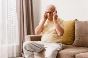 elderly man suffering from a headache while sitting on his couch